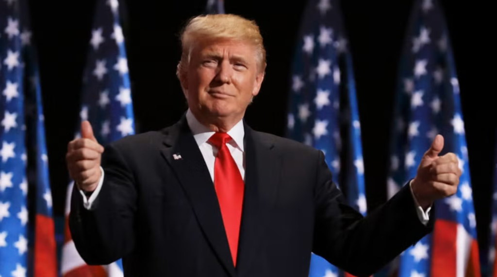 Donald Trump giving thumbs up in front of American flags